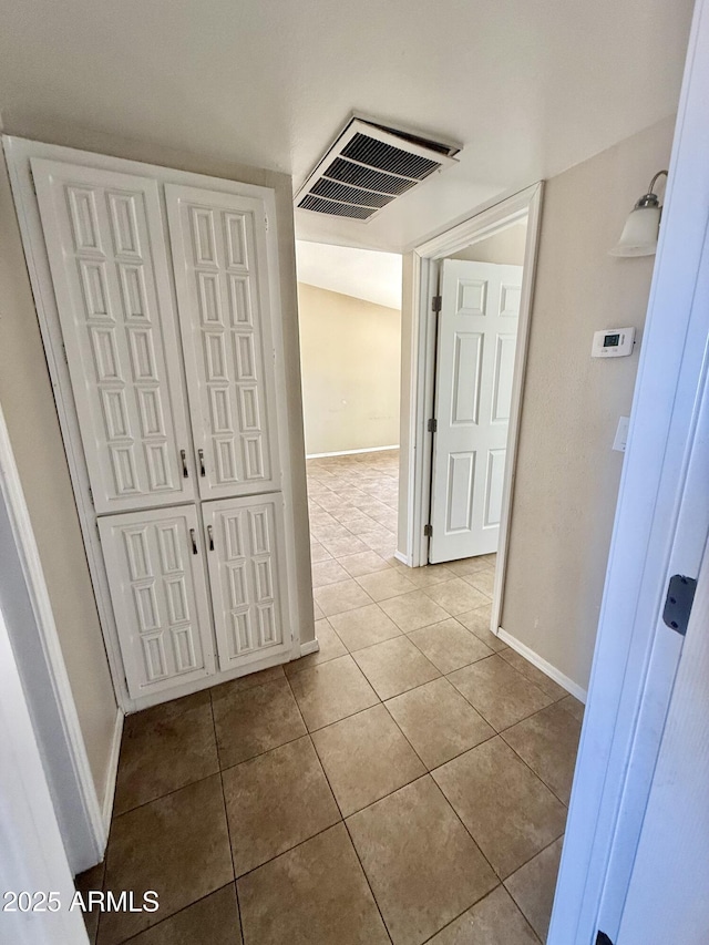 hall featuring baseboards, visible vents, and tile patterned flooring
