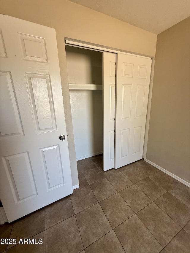unfurnished bedroom with dark tile patterned floors, baseboards, and a closet