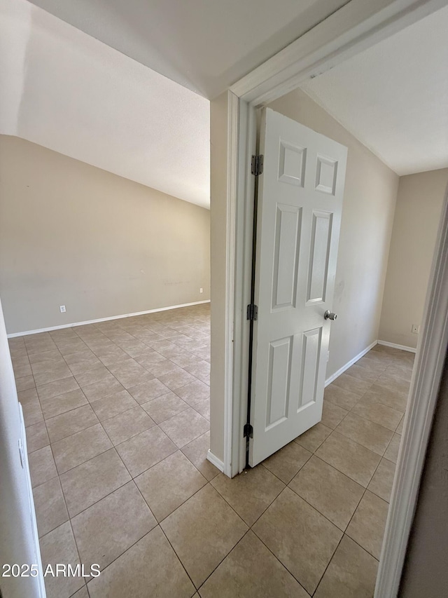 corridor with baseboards, lofted ceiling, and light tile patterned floors