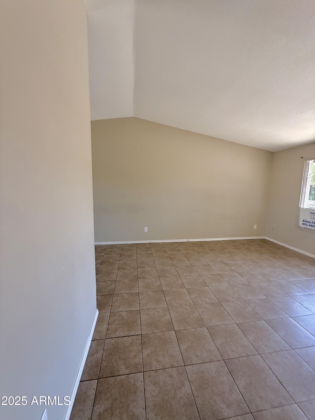 tiled spare room featuring baseboards and lofted ceiling