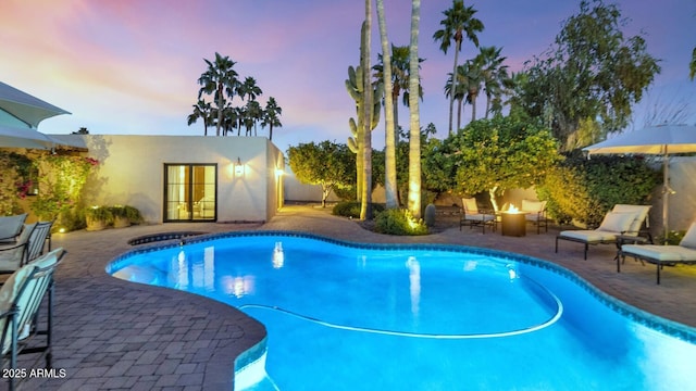 pool at dusk featuring an outdoor fire pit and a patio