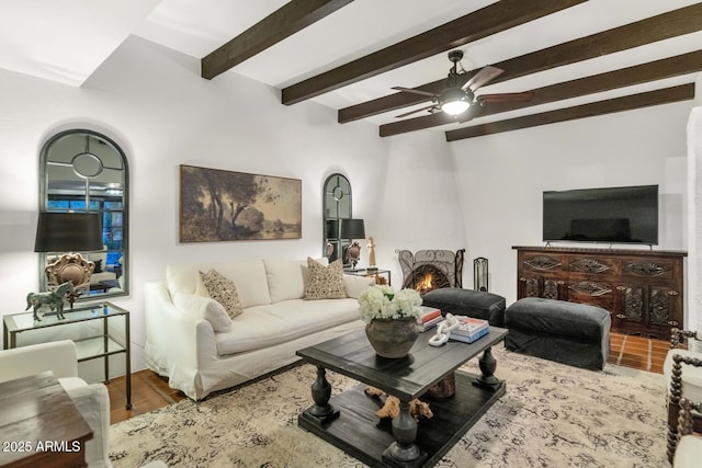 living room featuring wood-type flooring, a fireplace, ceiling fan, and beamed ceiling