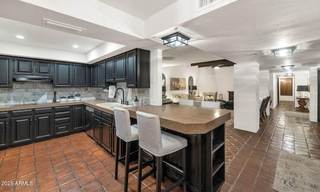 kitchen with a breakfast bar area, kitchen peninsula, dark tile patterned flooring, sink, and tasteful backsplash