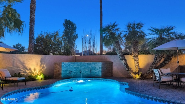 pool at dusk with pool water feature and a patio area