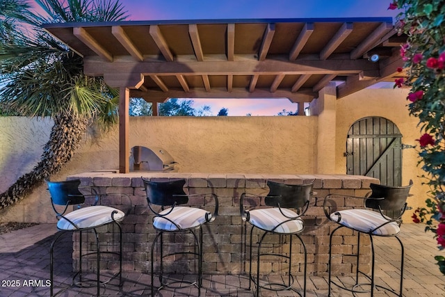 patio terrace at dusk featuring a bar and area for grilling