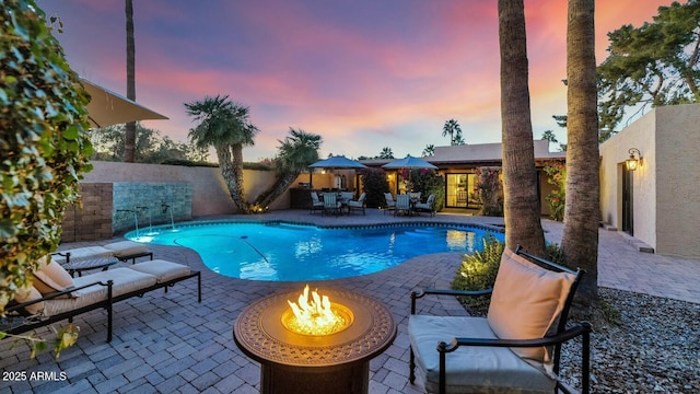 pool at dusk with a fire pit, pool water feature, and a patio area