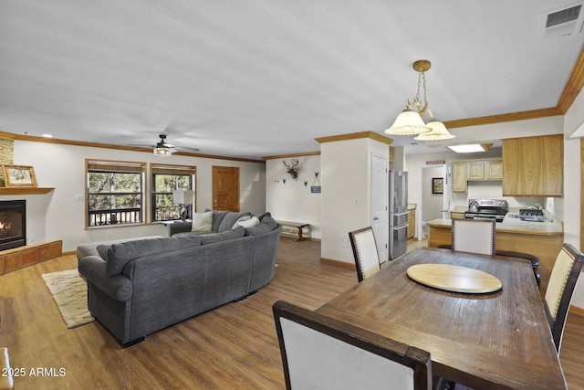 dining room featuring ornamental molding, light wood-type flooring, ceiling fan, and a fireplace