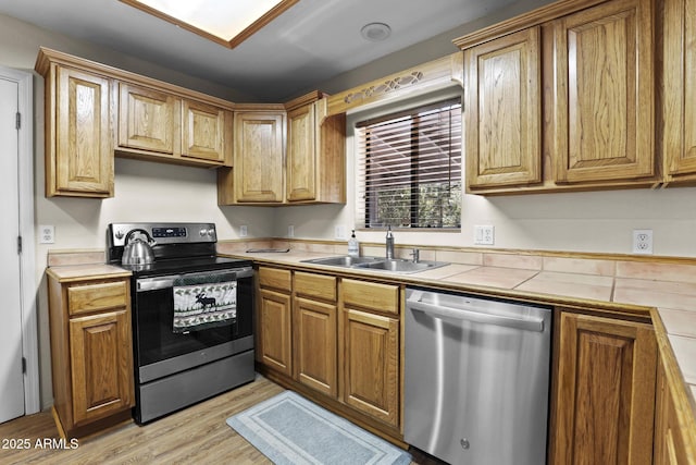 kitchen with appliances with stainless steel finishes, tile counters, sink, and light wood-type flooring