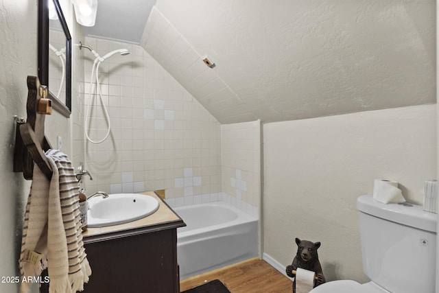 full bathroom featuring lofted ceiling, toilet, tiled shower / bath, wood-type flooring, and vanity