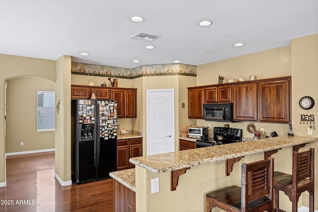 kitchen featuring visible vents, a kitchen bar, black appliances, dark wood-style floors, and a peninsula