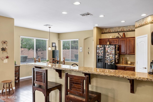 kitchen with visible vents, decorative light fixtures, light stone counters, a kitchen breakfast bar, and black fridge with ice dispenser