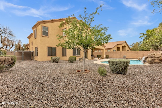 rear view of house with stucco siding, a gate, fence, a fenced in pool, and a tiled roof