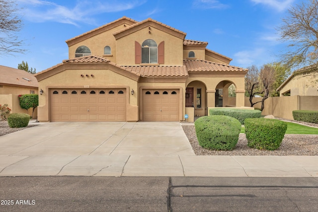 mediterranean / spanish home with a tiled roof, fence, driveway, and stucco siding