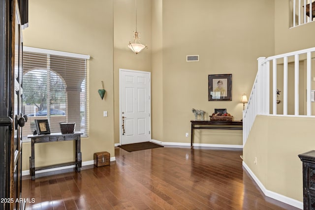 entrance foyer featuring baseboards, visible vents, dark wood finished floors, a high ceiling, and stairs