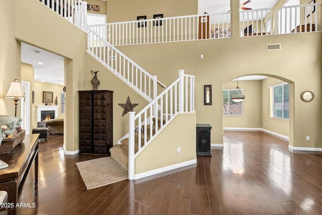 stairs featuring visible vents, baseboards, hardwood / wood-style floors, arched walkways, and a ceiling fan