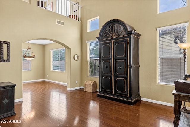 interior space featuring visible vents, arched walkways, dark wood-style flooring, and baseboards