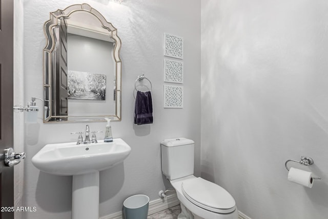 bathroom featuring baseboards, toilet, and a sink