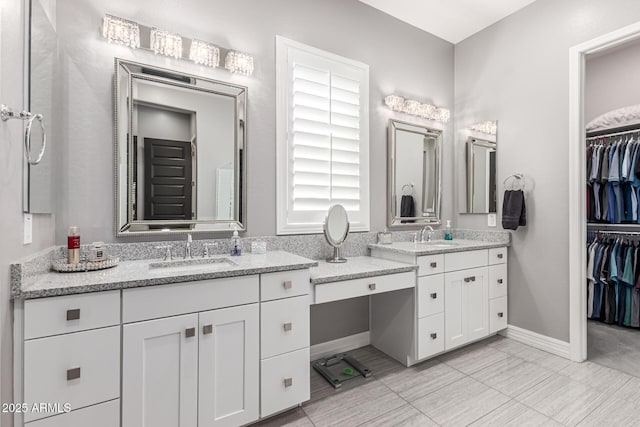 bathroom featuring baseboards, a sink, a spacious closet, and two vanities