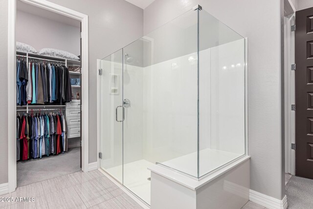 bathroom with a spacious closet, a stall shower, and baseboards