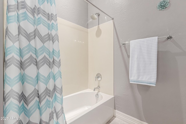 bathroom featuring shower / bath combo, a textured wall, and baseboards