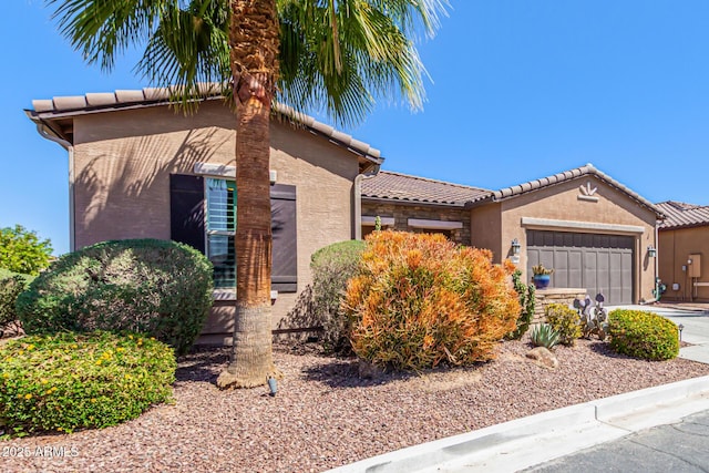view of front of house featuring an attached garage, a tile roof, stucco siding, and driveway