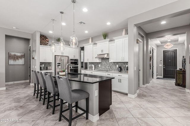 kitchen featuring a breakfast bar area, under cabinet range hood, an island with sink, visible vents, and appliances with stainless steel finishes