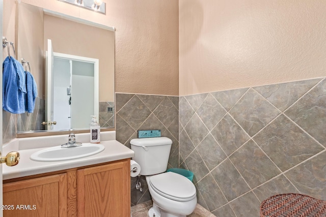 bathroom featuring toilet, tile walls, vanity, and a textured wall