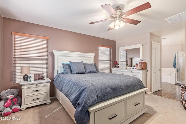 bedroom featuring a ceiling fan, light colored carpet, visible vents, and connected bathroom