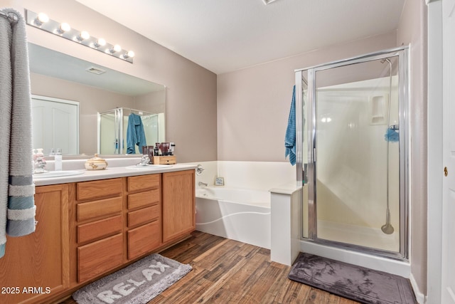 full bath with a bath, a shower stall, double vanity, and wood finished floors