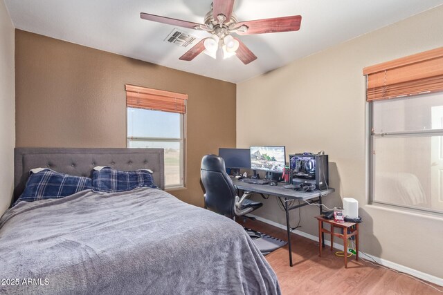 bedroom with ceiling fan, visible vents, baseboards, and wood finished floors