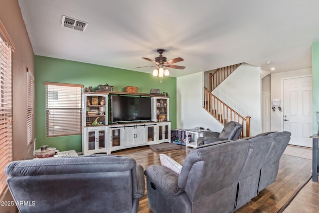 living room featuring stairs, visible vents, wood finished floors, and a ceiling fan