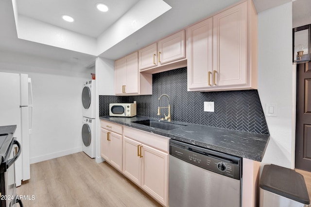 kitchen with light wood-type flooring, sink, stacked washing maching and dryer, white appliances, and dark stone countertops