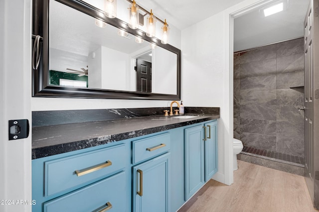 bathroom featuring a tile shower, wood-type flooring, vanity, and toilet