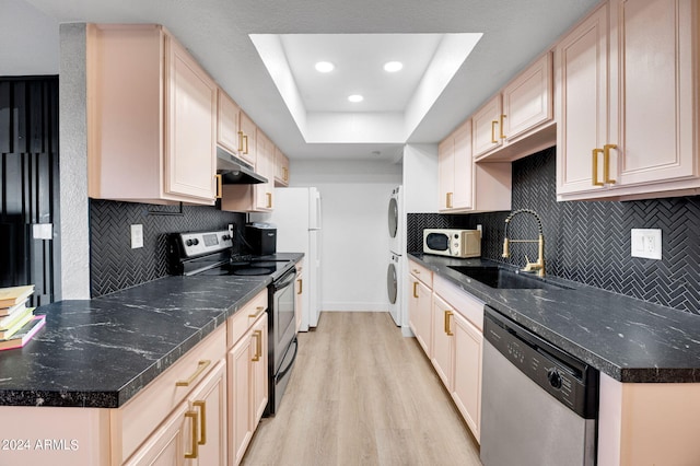 kitchen with light wood-type flooring, stacked washer / dryer, tasteful backsplash, sink, and appliances with stainless steel finishes