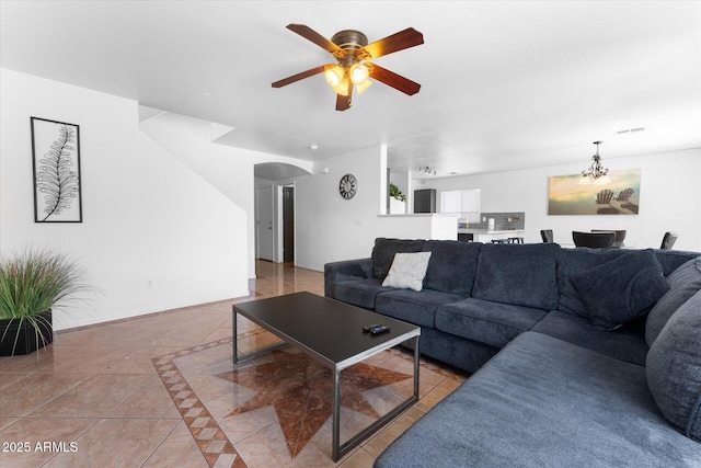 living area with baseboards, tile patterned flooring, visible vents, arched walkways, and ceiling fan with notable chandelier