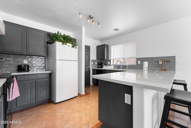 kitchen featuring a breakfast bar, a peninsula, freestanding refrigerator, backsplash, and a sink