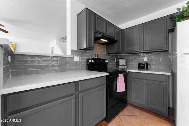 kitchen featuring tasteful backsplash, freestanding refrigerator, under cabinet range hood, black / electric stove, and gray cabinetry