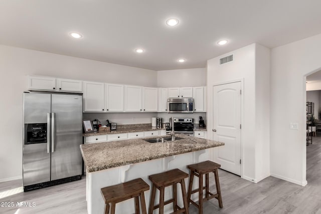 kitchen featuring appliances with stainless steel finishes, white cabinetry, a kitchen breakfast bar, a kitchen island with sink, and light stone counters