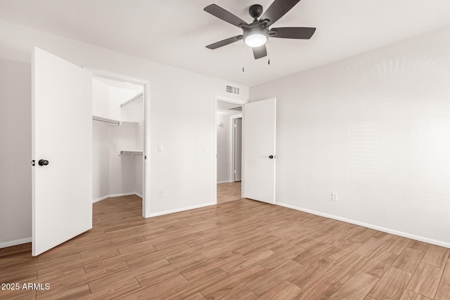 unfurnished bedroom featuring ceiling fan, a walk in closet, a closet, and light wood-type flooring