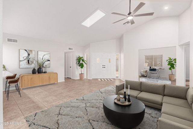 tiled living room featuring ceiling fan, a skylight, and high vaulted ceiling