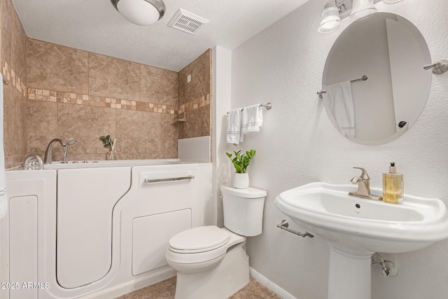 bathroom with toilet, washer / clothes dryer, a textured ceiling, and a washtub