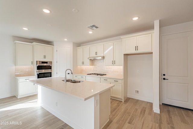 kitchen featuring decorative backsplash, stainless steel appliances, sink, a center island with sink, and white cabinetry