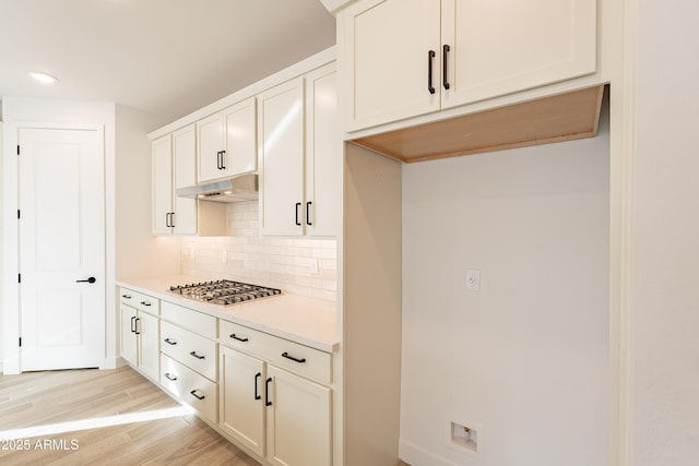 kitchen with decorative backsplash, light hardwood / wood-style flooring, white cabinets, and stainless steel gas stovetop