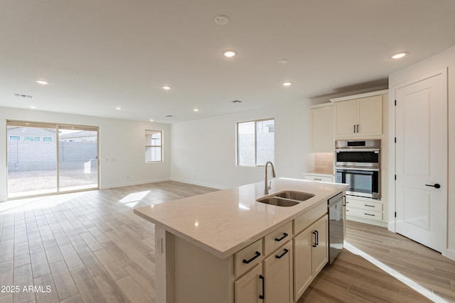 kitchen with sink, light stone counters, light hardwood / wood-style flooring, an island with sink, and appliances with stainless steel finishes