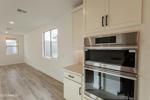 kitchen featuring plenty of natural light, light hardwood / wood-style floors, and stainless steel double oven