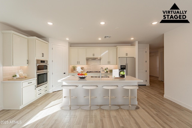 kitchen with a center island with sink, light hardwood / wood-style flooring, appliances with stainless steel finishes, a kitchen bar, and white cabinetry