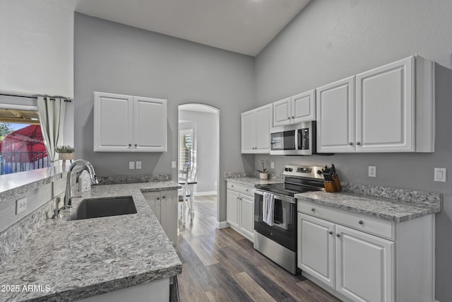 kitchen featuring a towering ceiling, white cabinetry, arched walkways, a sink, and appliances with stainless steel finishes