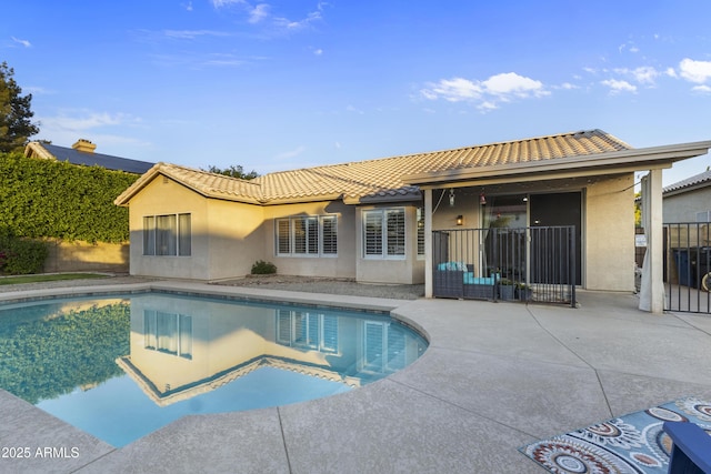 back of house featuring an outdoor pool, stucco siding, and a tiled roof