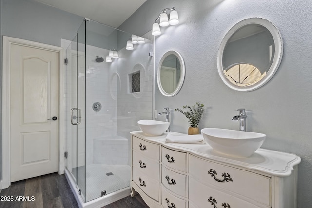 full bath with wood finished floors, double vanity, a sink, and a stall shower