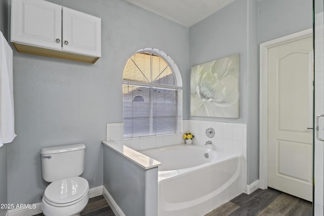 bathroom featuring toilet, baseboards, wood finished floors, and a bath